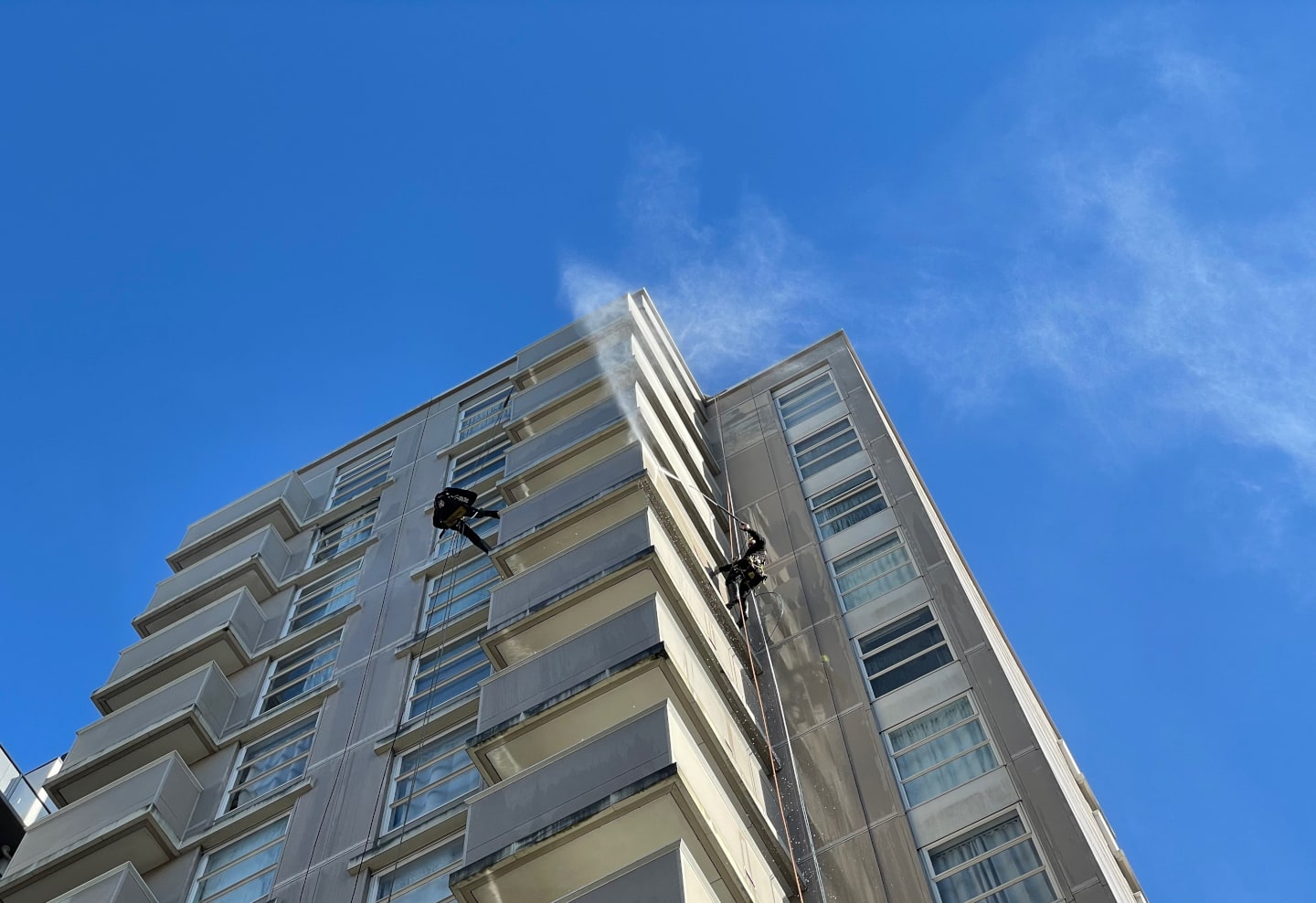 建筑墙面清洗喷出的水柱在蓝天下变成了雾。
