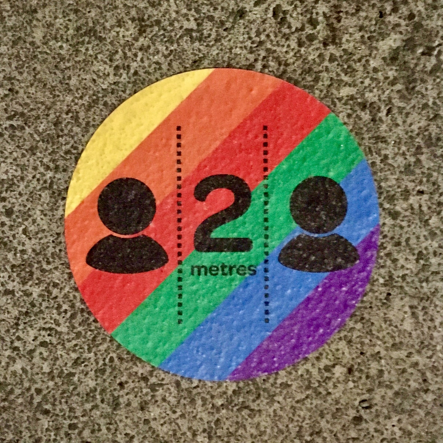A rainbow-coloured sticker on the street reminds people to maintain COVID-19 social distance.